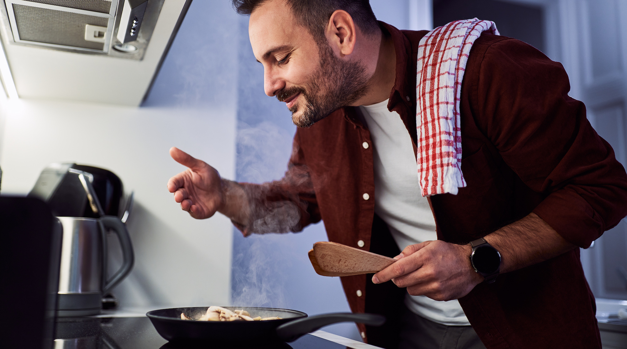 A man enjoying the aroma of his meal in a pan, cooking in his kitchen.
